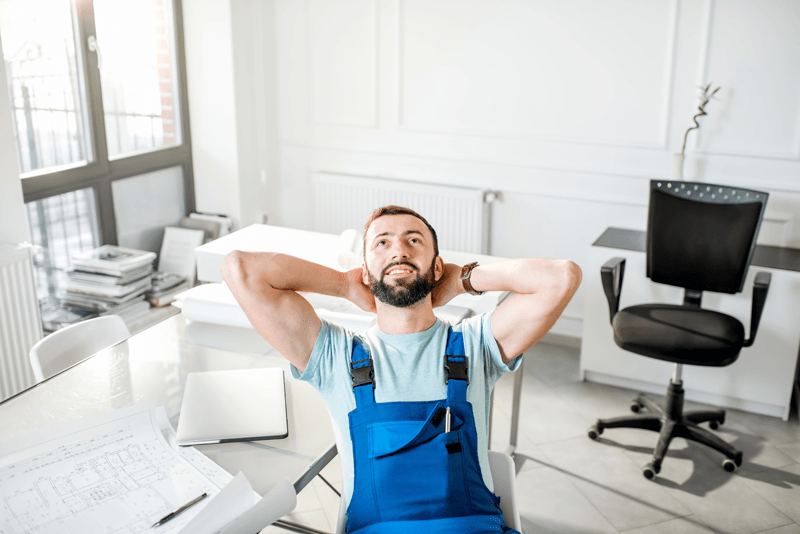 Ein Handwerker sitzt im Bürostuhl und lehnt sich entspannt und zufrieden zurück.